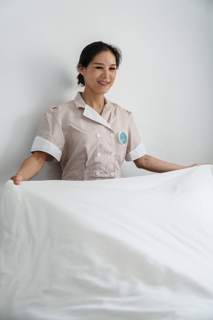 Smiling housekeeper changes bed linen in a clean, bright room. Ideal for hospitality and cleaning services imagery.